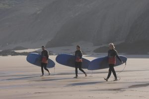 Group of surf students carrying surfboards on a beach in the Algarve in autumn