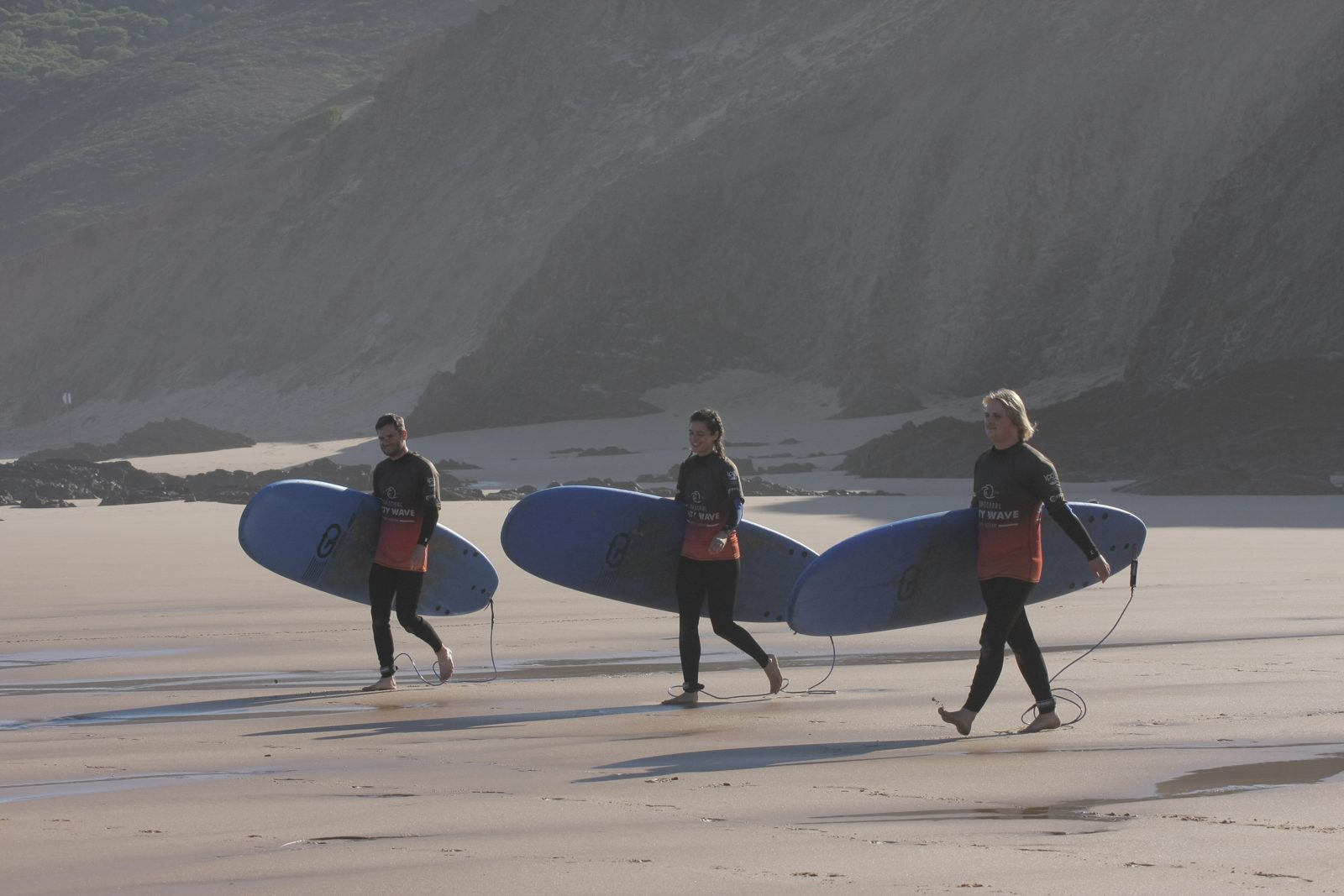 Group of surf students carrying surfboards on a beach in the Algarve in autumn